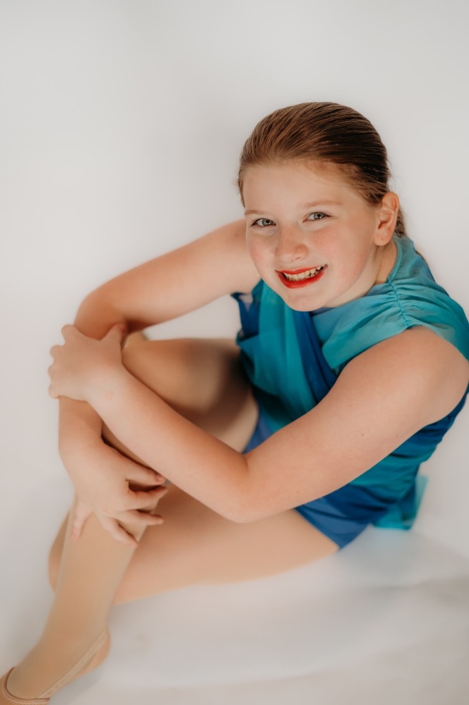 Young dancer in teal costume posed on white background